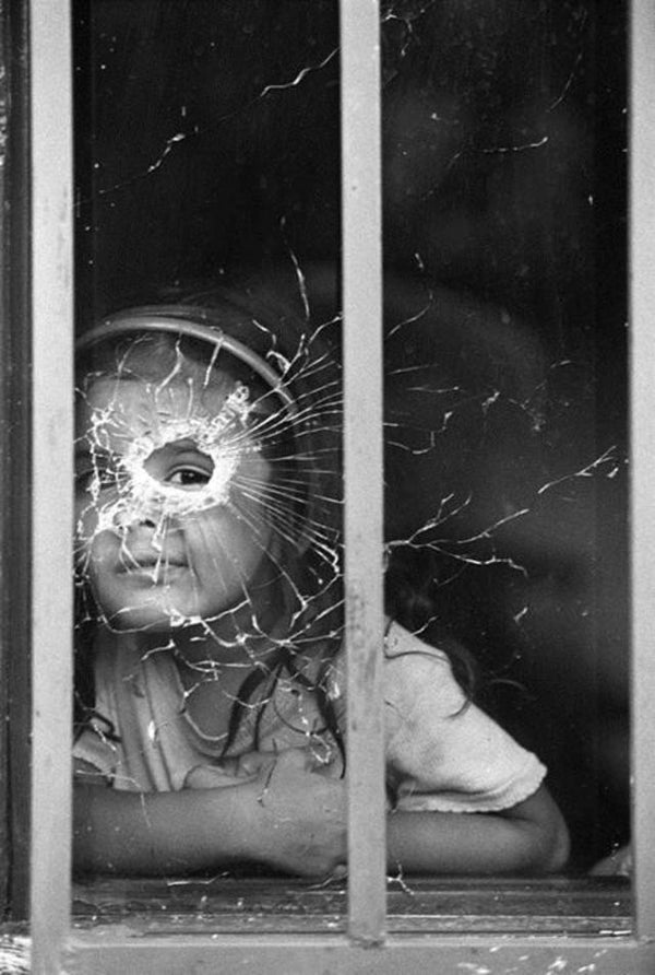 Fotografía de una niña colombiana mirando a través de un disparo en un cristal, por Jesús Abad Colorado